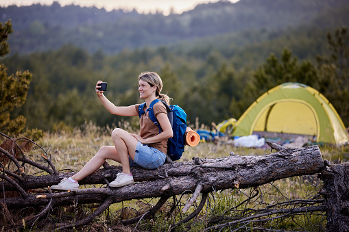 Happy female hiker having fun while taking a selfie with mobile phone during a break in nature. Copy space.