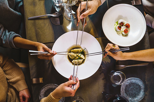 Group of people sharing Chinese steamed dumplings - zenithal view of the table with four hands holding chopsticks on fusion food luxury restaurant - people, food and drink concept - food photography lifestyle