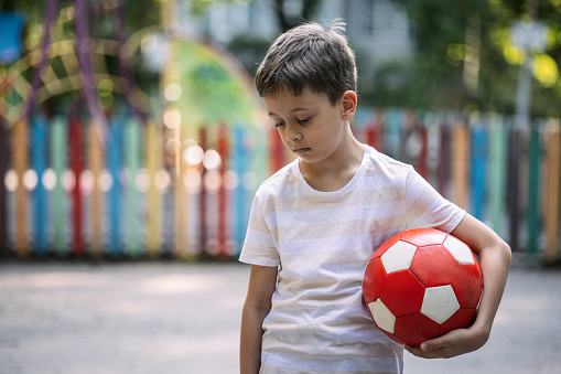 Sad kid holding ball and looking down