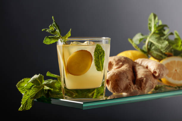 ginger ale beer cocktail with lemon and mint in a frozen glass on a black background. - ginger tea root hot drink foto e immagini stock