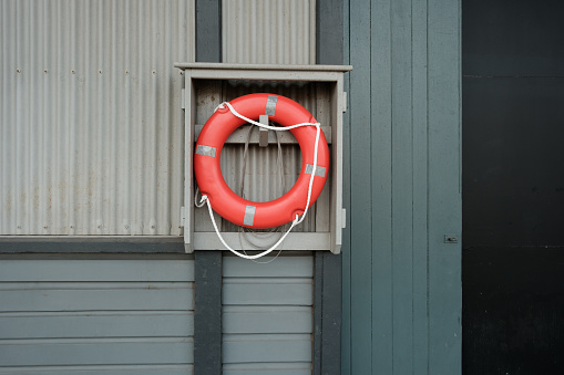 Orange lifebuoy with white rope on a wooden wall.