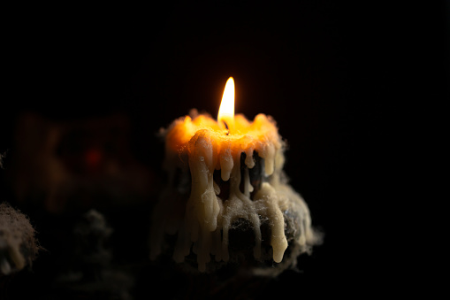 A burning candle in close-up, an antique candlestick covered with wax and cobwebs on a black background