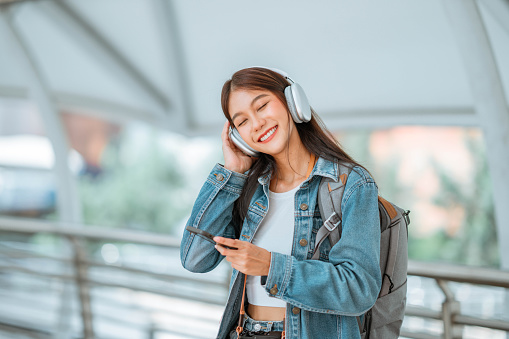 Happy young asian woman putting headphones and enjoying music on the urban city, Smiling female listening to music and dancing alone.