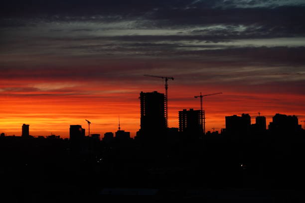 istock Sunset against the backdrop of a large construction site with several working cranes and unfinished high-rise buildings. Sunset with orange and red sky in cityscape with silhouettes of buildings 1921628216