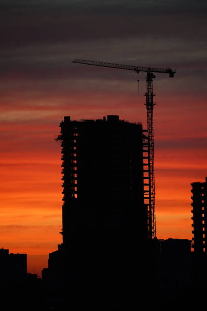 istock Sunset against the backdrop of a large construction site with several working cranes and unfinished high-rise buildings. Sunset with orange and red sky in cityscape with silhouettes of buildings 1921628217