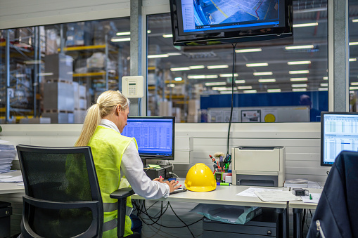 Female caucasian shipping operator managing orders on computer and digital tablet while working in warehouse office, medium shot