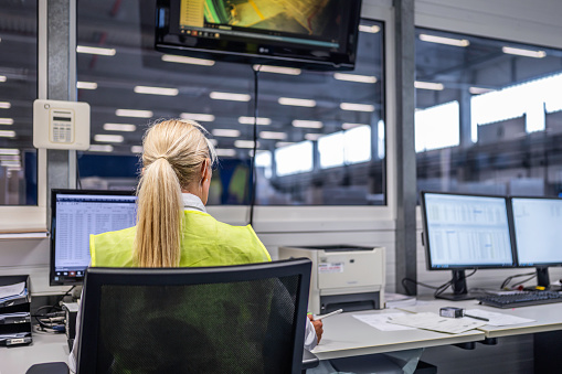 Female caucasian shipping operator managing orders on computer while working in warehouse office, medium shot back view