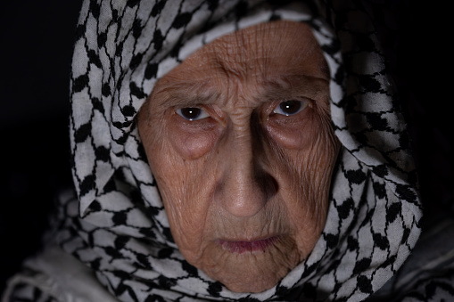 Portrait of old lady wearing white keffiyeh in dark with anger facial expression