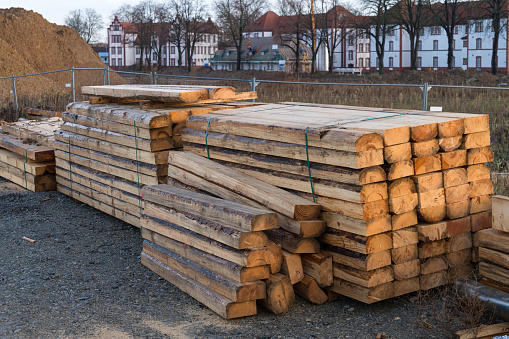 Sawing wooden beams stacked at a construction site.