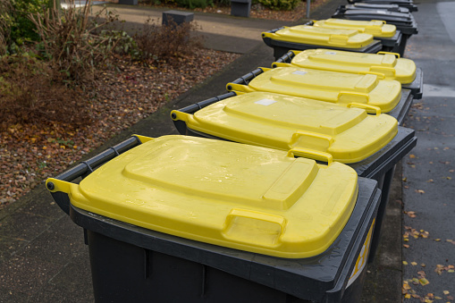 Yellow lids of plastic trash cans standing on the side of the road.