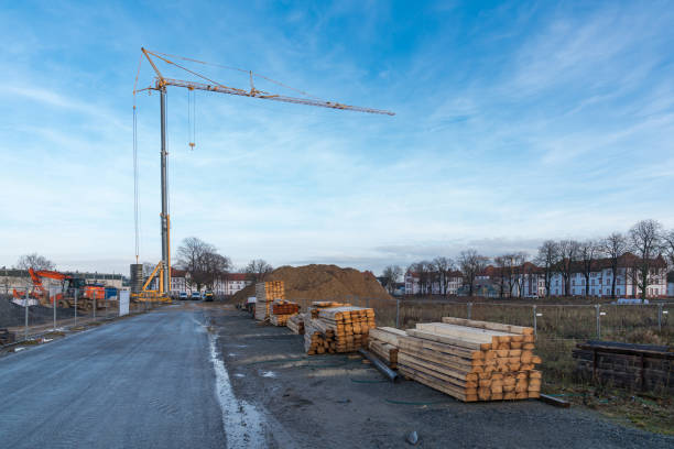 Tower crane and excavator on a construction site with stacked timber. Blue sky with light clouds