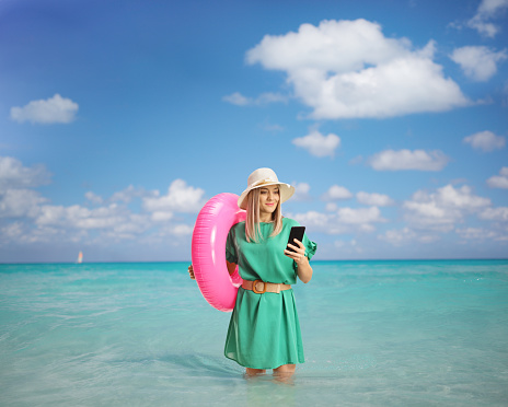 Young woman with a swimming ring browsing on a smartphone and standing inside a sea