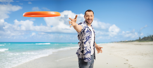 Cheerful young man throwing a flying disk on a sandy beach