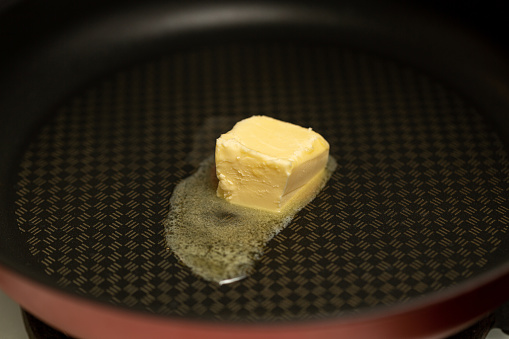 A piece of butter is melted in a non-stick frying pan, close-up