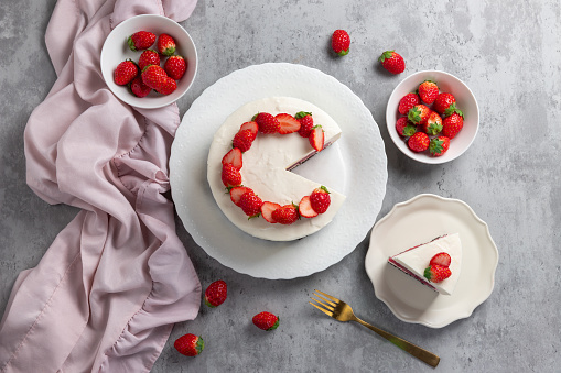 No bake cheesecake with fresh strawberries on top on a white plate on a gray concrete background.