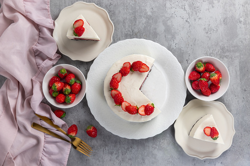 No bake cheesecake with fresh strawberries on top on a white plate on a gray concrete background.