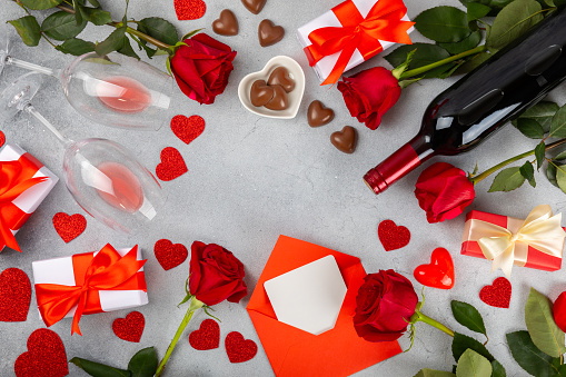 Valentine's Day concept. Valentine's Day background. Gifts, candles, confetti, envelope - postcard, sweets, glasses, wine and a bouquet of roses on background. Flatley, top view.