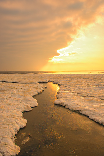 Arctic ice and sea panoramic landscape on the sand flats in the Waddensea at Schiermonnikoog island during a cold winter sunset.