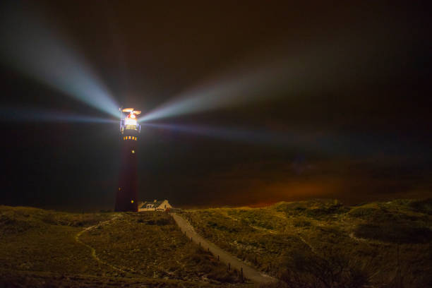 Lighthouse and fishermen's cottages in the night at the island of Schiermonnikoog in the Dutch Waddensea region in the North of The Netherlands. A path is leading up the dunes towards a lighthouse.