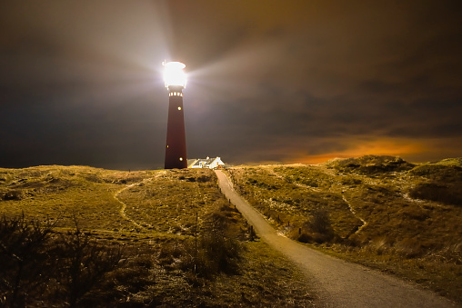 Lighthouse and fishermen's cottages in the night at the island of Schiermonnikoog in the Dutch Waddensea region in the North of The Netherlands. A path is leading up the dunes towards a lighthouse.