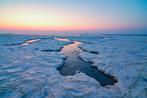 Arctic ice and sea panoramic landscape on the sand flats in the Waddensea at Schiermonnikoog island during a cold winter sunset.
