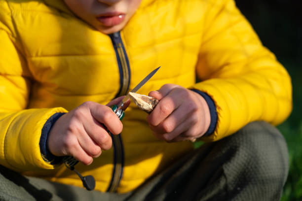 Boy sharpening a stick to make an arrow with a utility knife