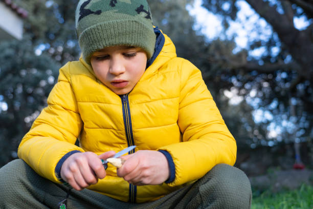istock Concentrated boy making a spear with a stick and a utility knife 1921728967