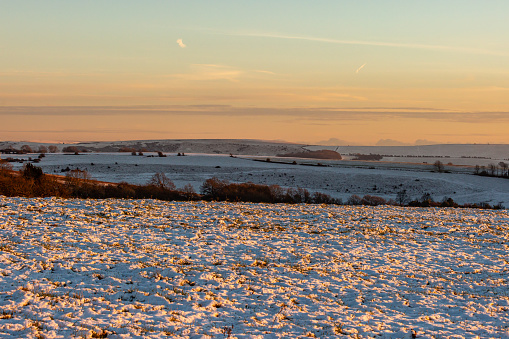A winter view on Ditchling Beacon in Sussex with a sunset sky glowing on the snow covered fields