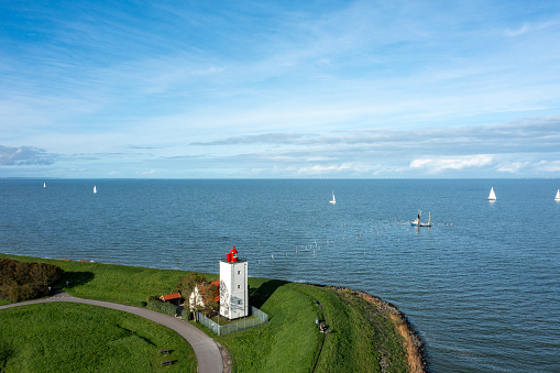 View of one fisher boat approaching the lighthouse of Andijk, on the horizon some sailboats. drone shot.