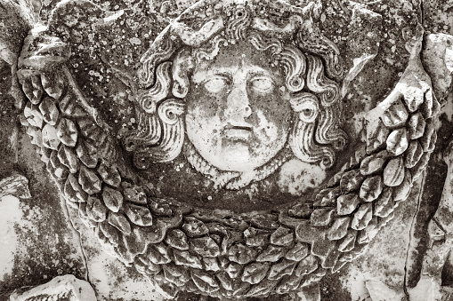 The face and wings of a carved face of a winged angel on an ancient gravestone on Burial Hill in Plymouth, Massachusetts.