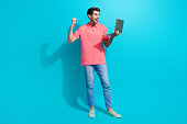 Photo of young successful businessman raised fist up using macbook pro and enjoying fast montage isolated on cyan color background