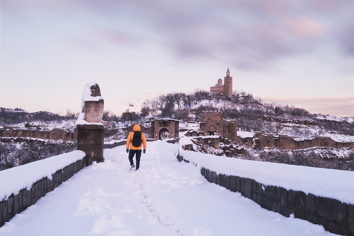 Young adult man wearing yellow jacket and a backpack is exploring a castle in the winter. Tsarevets fortress, Veliko Tarnovo, Bulgaria
