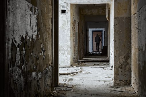 A man stands in an abandoned corridor. Rear view of man standing in corridor at abandoned building