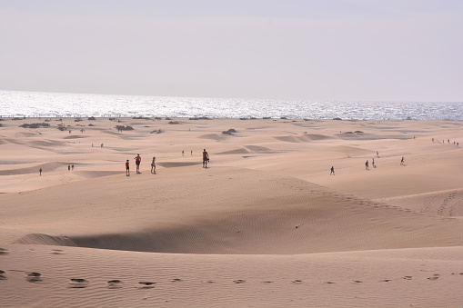Maspalomas, Spain - December 09, 2023: People under orange beach umbrellas on the beach in Maspalomas