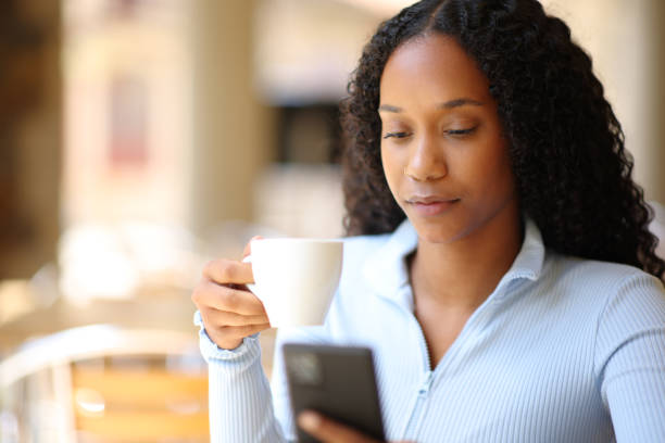istock Black woman drinking coffee checking phone 1921903185