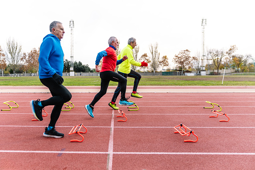 A trio of elderly men engaging in agility training with colorful hurdles on an athletic track