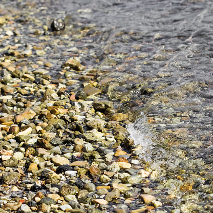 Background of sandy, stones and flowing waves on the sea beach. Summer holidays and coastal nature concept