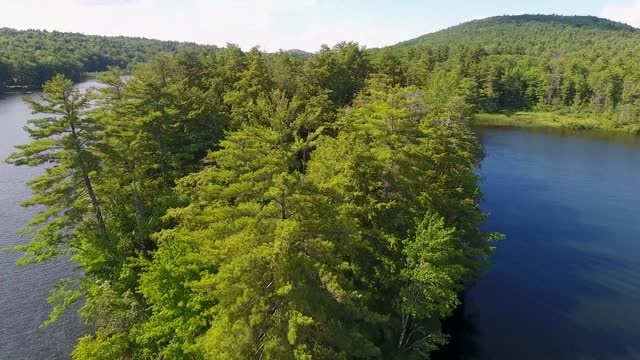 A spectacular 4K drone shot over Parker Pond and Pleasant Lake, located in Casco, Maine, USA. The camera moves low over the surface of the water, then rises and pans down over a forested peninsula.