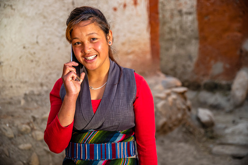 Tibetan young woman using mobile phone, Lo Manthang, Upper Mustang. Mustang region is the former Kingdom of Lo and now part of Nepal,  in the north-central part of that country, bordering the People's Republic of China on the Tibetan plateau between the Nepalese provinces of Dolpo and Manang.