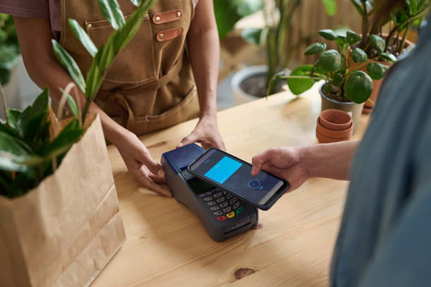 istock Woman Using Modern Technology to Pay for Potted Plant in Store 1921980981