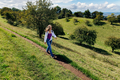 Teenage girl is hiking in the Cotswolds, Worcestershire, United Kingdom. She is walking on the footpath on beautiful green hills.
Sunny and cloudy, summer day.
Shot with Canon R5