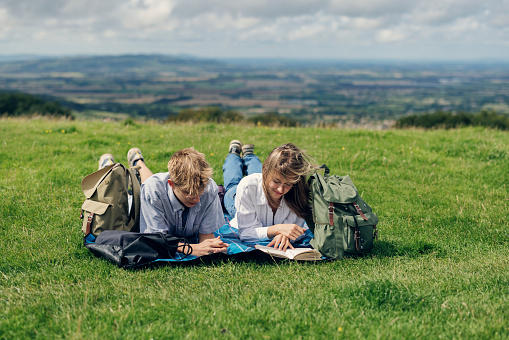Three teenage kids are hiking in the Cotswolds, Worcestershire, United Kingdom. They enjoying a short break, lying on a blanket and reading a book and using phones.
Overcast, summer day.
Shot with Canon R5
