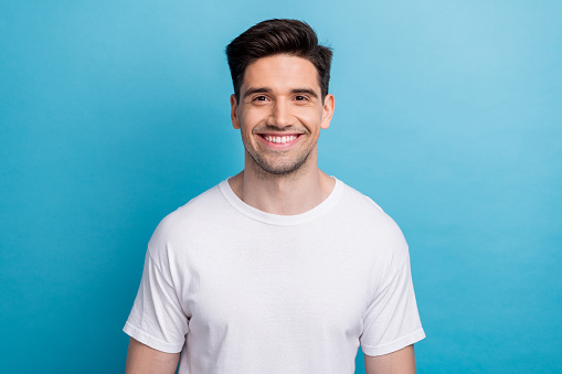 Photo of good mood cheerful guy wear white t-shirt smiling showing teeth isolated blue color background.