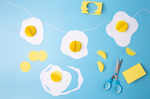 fried eggs paper craft on a blue background, Easter decoration concept, art project for kids, how to make an egg garland, DIY