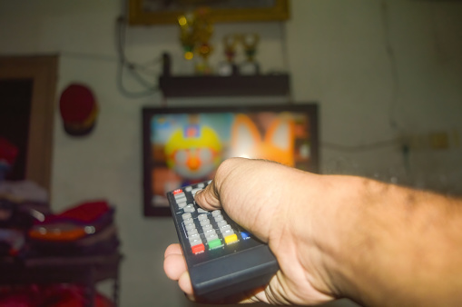 The hand is holding the TV remote in front of a television, preparing to change the TV channel
