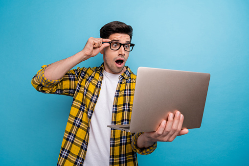 Photo of astonished man dressed plaid shirt touch eyewear staring at unbelievable sale in laptop isolated on blue color background.