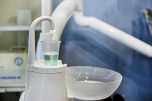 disposable cup with liquid for rinsing teeth in a dental office on a light background. Dental care and treatment