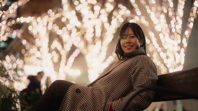 Portrait of Asian woman sitting under Christmas illumination lights in city at night