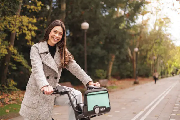 Portrait of smiling young latin woman riding an electric-bike in a park. High quality photo
