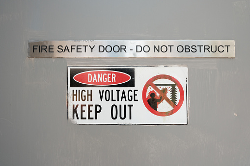 Danger, high voltage, keep out sign on a gray door.